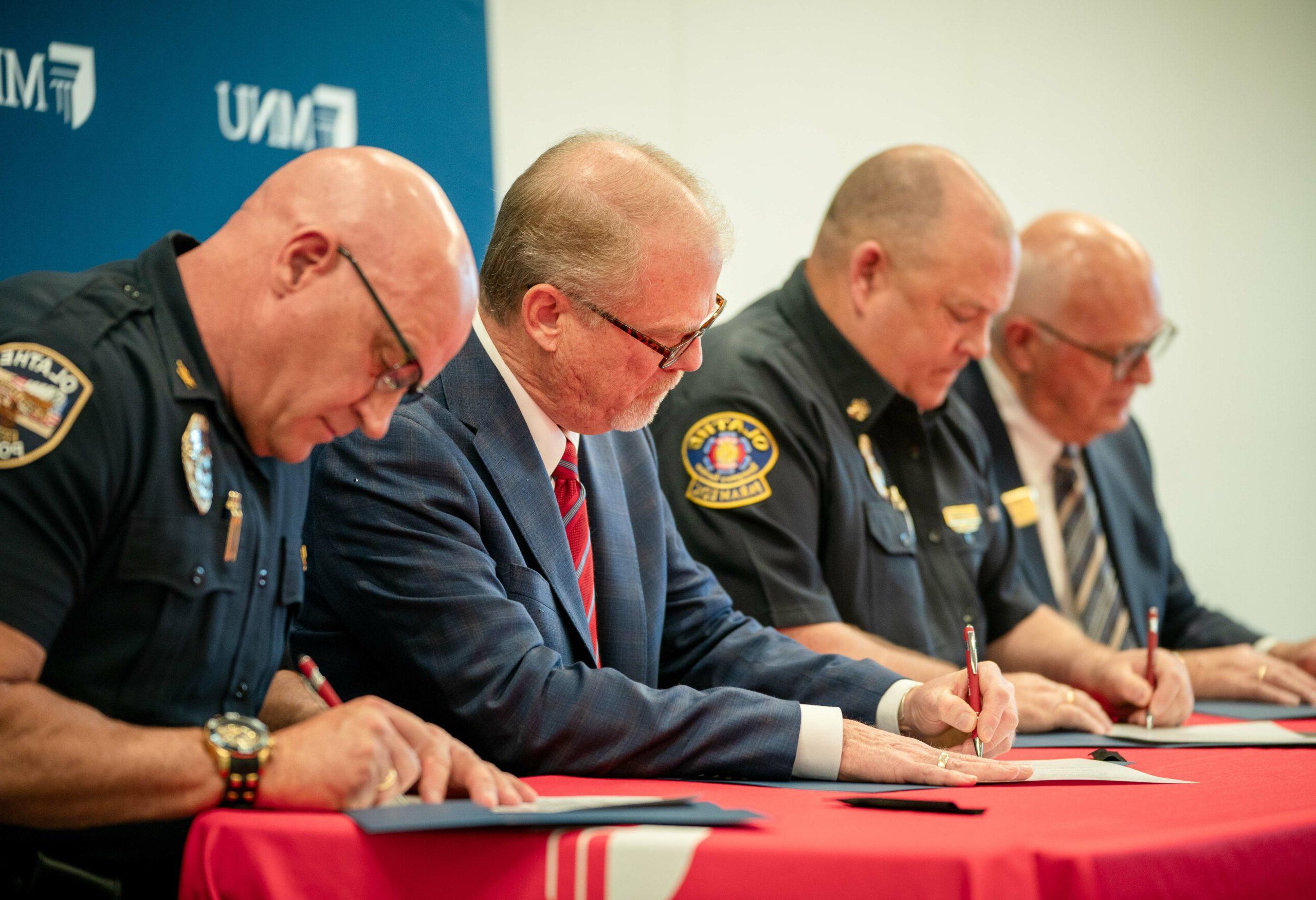 MNU President David Spittal, Fire Chief Jeff DeGraffenreid, 市长约翰·贝肯和警察局长迈克·布托签署奖学金协议